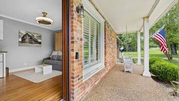 A covered porch with a brick wall, a white bench, and an American flag.
