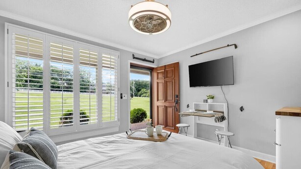 Ein Schlafzimmer mit einem großen Bett, einem an der Wand montierten Fernseher und einer Glastür zum Garten.