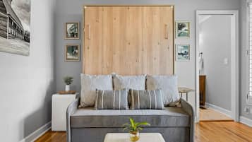 A modern living room with a grey sofa, a wooden wardrobe, and framed pictures on the wall.