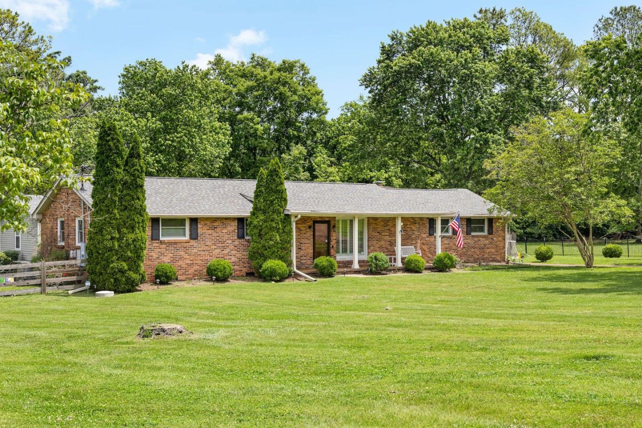 A brick house with a front porch, surrounded by a well-maintained lawn and trees.