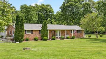 A brick house with a front porch, surrounded by a well-maintained lawn and trees.