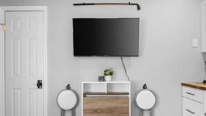 Ein modernes Zimmer mit einem an der Wand befestigten Flachbildfernseher, einem kleinen Holzschrank, zwei weißen Hocker und einer weißen Tür.