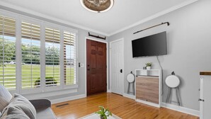 Ein Wohnzimmer mit einer Couch, einem Couchtisch mit Pflanze, einem Kamin und einem an der Wand montierten Fernseher.