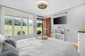 Un dormitorio con una cama grande, televisor montado en la pared y una puerta corrediza de vidrio que da a un jardín.