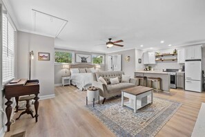 Een moderne, goed verlichte woonkamer met een bank, salontafel en een eethoek, met een keuken op de achtergrond.