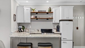 Una cocina moderna con armarios blancos, encimera de mármol, cocina integrada y refrigerador.