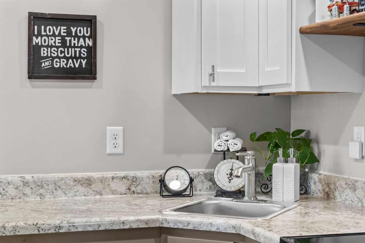 A kitchen with a marble countertop, a sink, a scale, a clock, and a sign saying "I LOVE YOU MORE THAN BISCUITS AND GRAVY".