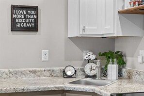 Una cocina con encimera de mármol, un lavabo, una balanza, un reloj y un cartel que dice "I LOVE YOU MORE THAN BISCUITS AND GRAVY".