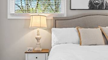 A bedroom with a bed, a bedside table with a lamp, a nightstand, and a window with blinds.