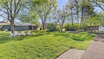 A well-maintained grassy yard with white outdoor furniture and a fire pit, surrounded by trees and a small shed.