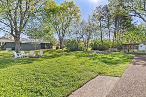 A well-maintained grassy yard with white outdoor furniture and a fire pit, surrounded by trees and a small shed.