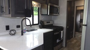 A compact kitchen with a microwave, stove, and sink. - The Castle at Rock Castle (Cadiz)