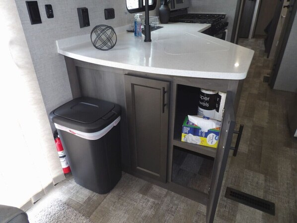 A compact kitchen with a white countertop, a trash bin, a cabinet with a shelf, and a fire extinguisher. - The Castle at Rock Castle (Cadiz)
