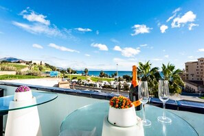 A balcony with a glass table, a bottle of champagne, and two glasses, overlooking a coastal area with buildings and greenery. - Los Chopos - Townhouse in El Castillo Fuengirola (Fuengirola)