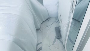 Un couloir étroit, avec un lit sur la gauche, une porte sur la droite et un sol carrelé à motifs de marbre.