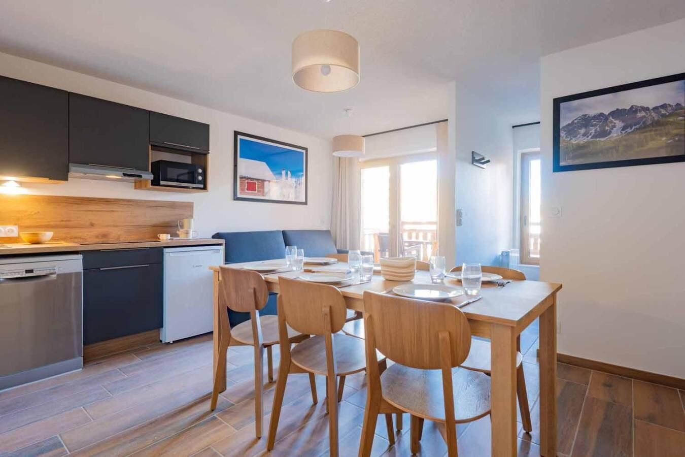A compact kitchen with modern appliances, a dining area with wooden chairs, and a large window offering a view.