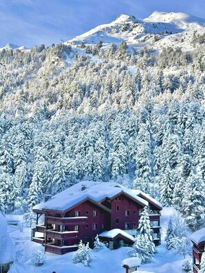 A red building with multiple balconies, surrounded by snow-covered trees and a mountain in the background. - 200m from ski slopes, 2nd floor, terrace, fireplace or stove, ski locker, 62m², Méribel-Mottaret (Méribel - Les Allues)