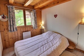 Una habitación de madera con una cama, una ventana con cortinas, una decoración con forma de corazón y una lámpara de noche.