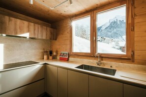 A modern kitchen with wooden cabinets, a stainless steel sink, and a window offering a view of a snowy mountain landscape.