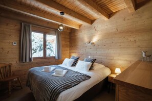 A cozy wooden cabin bedroom with a large bed, two bedside tables, a window with curtains, and a hanging light fixture.