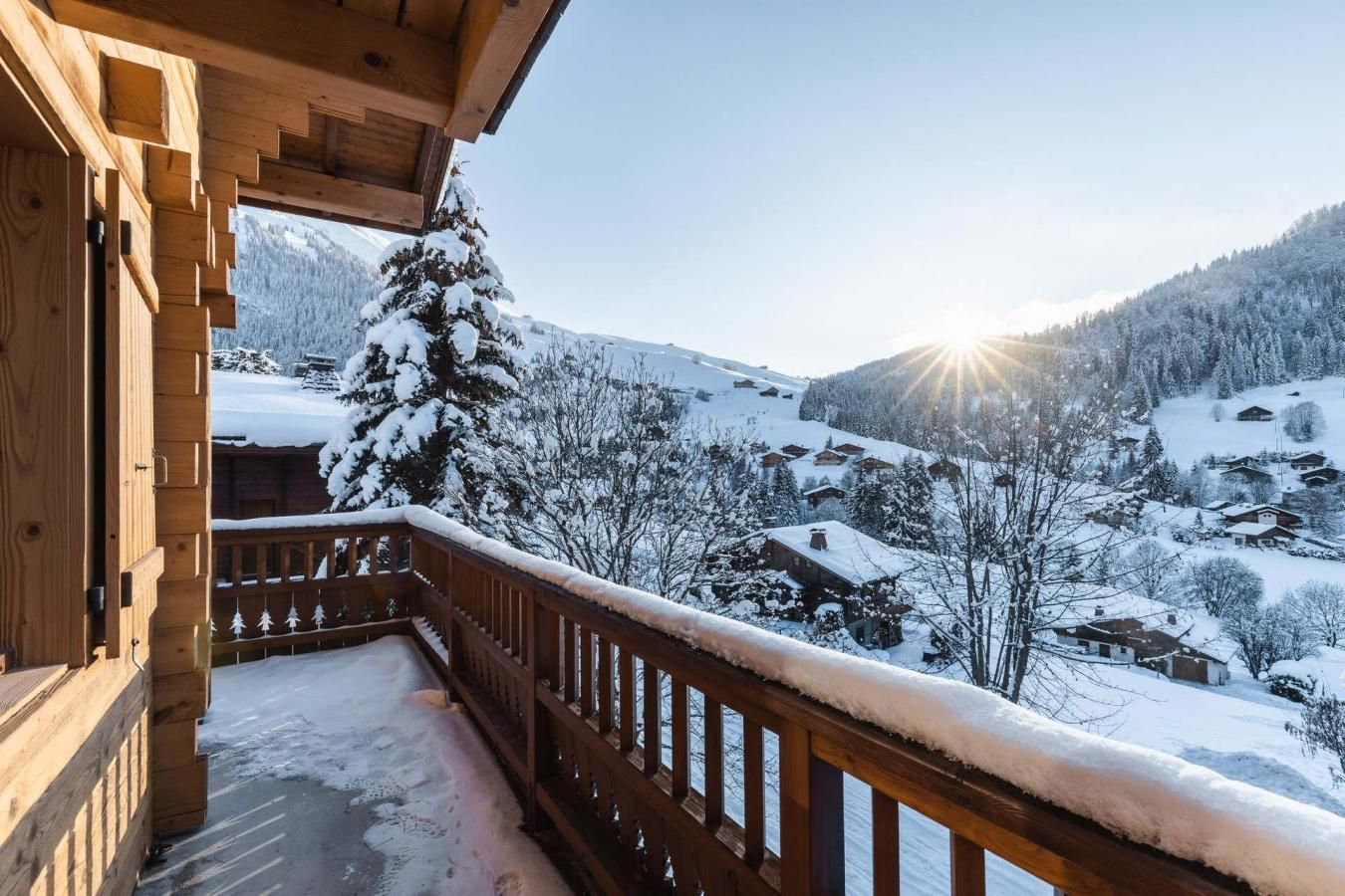 Un balcón de madera con vistas a un pueblo cubierto de nieve y montañas.