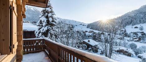 Un balcón de madera con vistas a un pueblo cubierto de nieve y montañas.