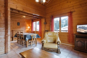 Ein Holzblockbau-Innenraum mit Esstisch, Stühlen, einem Ledersessel, einem Fernseher und einem Kamin.