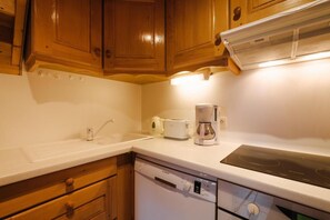 Cozinha com armários de madeira, bancada branca, cafeteira, torradeira e lava-louças.