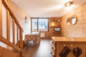A cozy wooden cabin interior with a dining table, chairs, a TV, and a kitchen area.