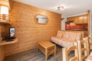 Ein Holzinnenraum mit einer Couch, einem kleinen Tisch, einem Fernseher und einer Küchenzeile.