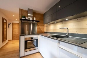 A modern kitchen with a built-in oven, stainless steel range hood, and a double sink.