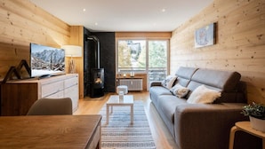 A cozy living room with a fireplace, wooden walls, a sofa, a TV, and a dining area.