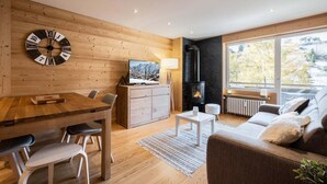 A cozy living room with a wooden wall, a fireplace, a TV, and a sofa.