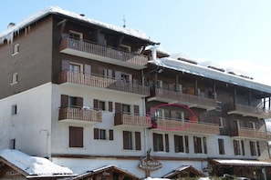 Um edifício de vários andares com varandas, um letreiro para 'La Gracia Eat-Restaurant' e neve no telhado e no chão.