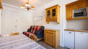 A compact room with a bed, a sofa, a wooden cabinet, a microwave, and a dishwasher.