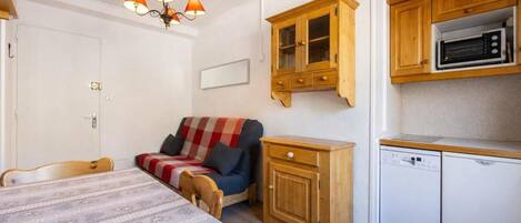 A compact room with a bed, a sofa, a wooden cabinet, a microwave, and a dishwasher.