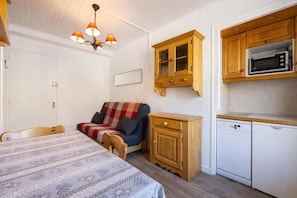 Quarto compacto com cama, sofá, armário de madeira, micro-ondas e lava-louças.