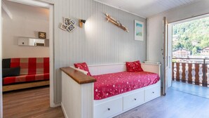 A cozy room with a wooden bench, a red bed with drawers, a wooden wall, and a balcony with a railing.