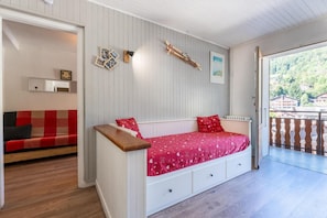 Quarto acolhedor com um banco de madeira, cama vermelha com gavetas, parede de madeira e varanda com guarda-corrimão.