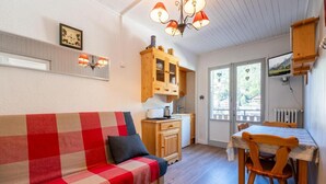 A cozy room with a checkered sofa, wooden cabinets, a dining table with chairs, and a kitchen area.