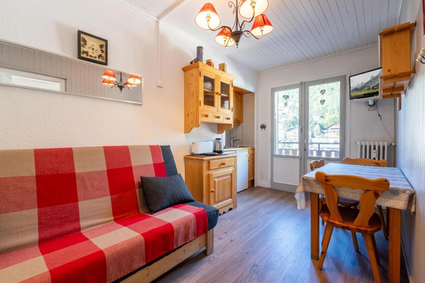 A cozy room with a checkered sofa, wooden cabinets, a dining table with chairs, and a kitchen area.