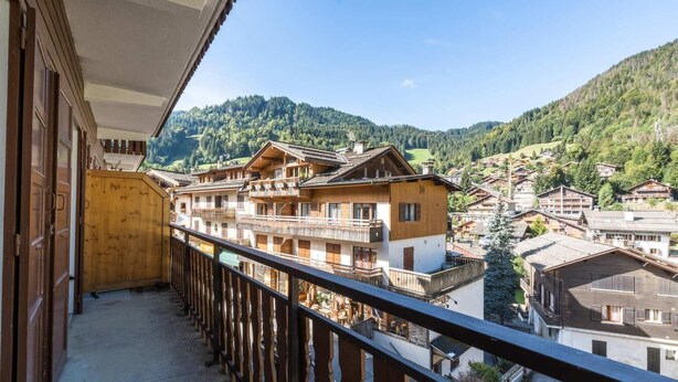 A balcony with a view of traditional wooden buildings and a forested mountain in the background.