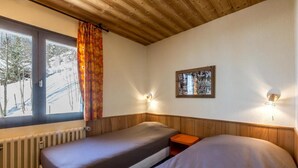 A room with two beds, a window with curtains, a radiator, and a wall-mounted picture.