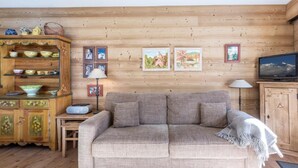 A cozy living room with a wooden wall, a sofa, a TV, and a cabinet with decorative items.