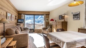 A cozy room with a wooden interior, a sofa, a dining table, and a view of snowy mountains.