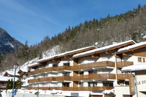 A multi-story hotel with wooden balconies and snow-covered roofs, set against a backdrop of a forested mountain.