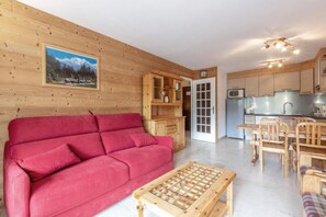 A cozy cabin interior with a red sofa, wooden dining table, and a kitchen area.