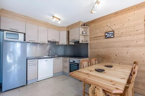 A compact kitchen with modern appliances, wooden wall paneling, and a dining table with chairs.