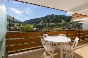A balcony with a white table and chairs, overlooking a mountainous landscape with houses and a church.