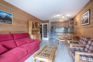 Ein gemütliches Interieur mit einem roten Sofa, einem karierten Sofa, einem Holztisch und einer Küchenzeile mit Schränken und einer Mikrowelle.